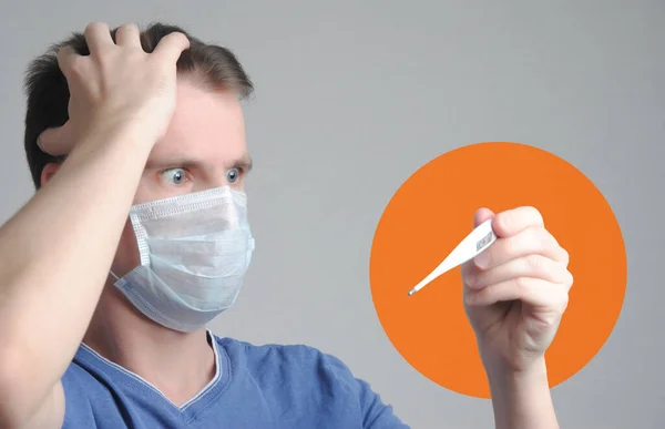 Een Man Met Een Medisch Masker Kijkt Naar Een Thermometer — Stockfoto
