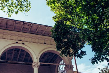 Ağaçların ve mavi gökyüzünün arka planında kemerler olan eski beyaz bir evin cephesi