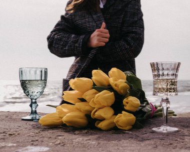 Bir buket sarı lale ve iki kadeh hafif şarap önlüklü ve denizde yaşayan bir kızın arka planına karşı.
