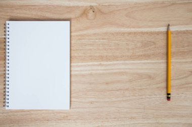 Tahta masanın üzerinde not defteri olan sarı kalem.