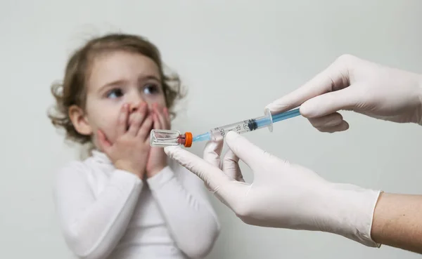 O médico segurando seringa hipodérmica, menina assustada no fundo. Foco seletivo e imagem tonificada — Fotografia de Stock