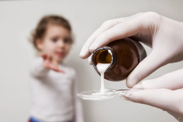 Girl awaits her medication pouring in a spoon in the foreground — Stock Photo, Image