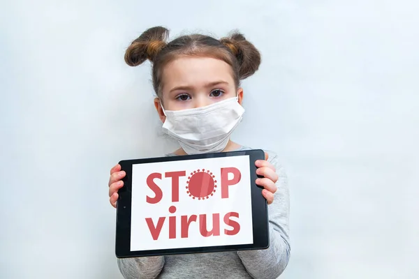 Ein kleines Mädchen in medizinischer Maske zeigt die Tablette mit der Aufschrift STOP VIRUS. Schutz vor Coronavirus-Epidemie — Stockfoto