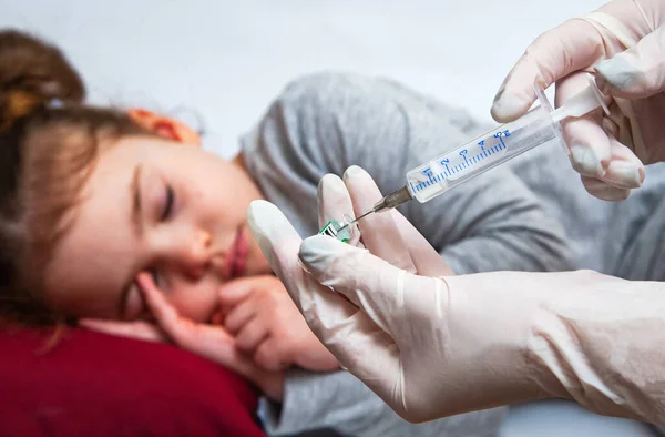 A enfermeira tem uma seringa para injectáveis para a menina. Um médico com luvas médicas prepara uma seringa . — Fotografia de Stock