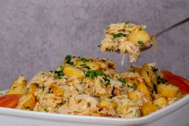 Bir kaşık morina sütyeni - geleneksel Portekiz yemeği, rendelenmiş morina balığı, patates ve soğan. Gri arka planda beyaz çanak çömlekle..