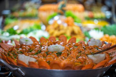 Ön planda deniz ürünleri paella 'sı ve arka planda açık büfe restoran yemekleri..