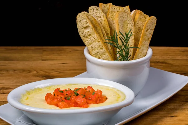 Baked cheese - melted cheese accompanied by bread toast, served in a white bowl on wooden board. Restaurant food concept. Food photography