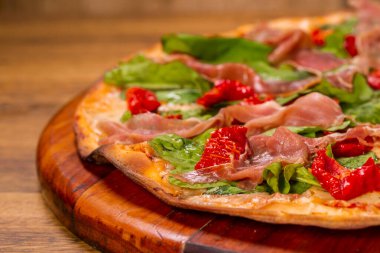 Kurutulmuş domatesli roka ve ahşap arka planda parma jambonlu pizza..