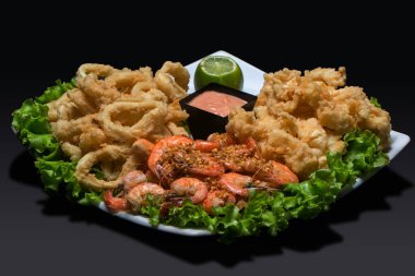 Siyah zemin üzerinde sos ve limonla servis edilen kalamar, karides ve balık kroketleri.