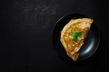 Siyah arka planda iştah açıcı sarı bir omlet resmi. Metni koymak için yer var. Sokak yemeği, yukarıdan görüntü