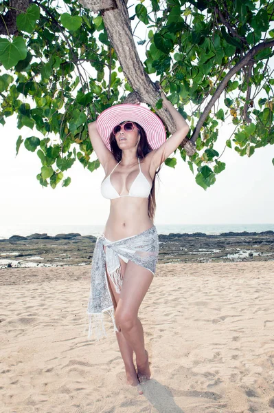 Mujer asiática bonita posando relajarse bajo el árbol en la playa con sombrero rosa . —  Fotos de Stock