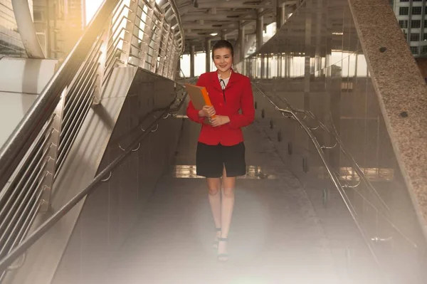 Asian Pretty woman in red suit holding document  walking on crossing bridge. — Stock Photo, Image