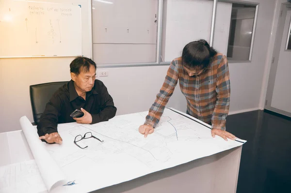 Architect and construction engineer or surveyor discussing plan and map in office room.