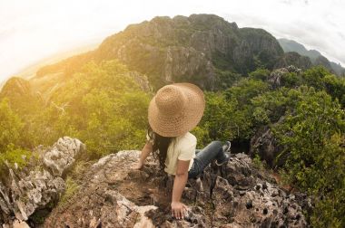 Bir dağın tepesinde oturan şapkalı kadın mutlu traveler.