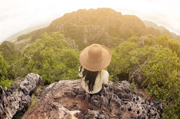 Gärna kvinnliga resenären med hatt som sitter ovanpå ett berg. — Stockfoto