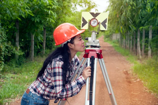 Vrouwelijke Surveyor of ingenieur maken stellen maatregel door prism reflector op straat in een veld. — Stockfoto