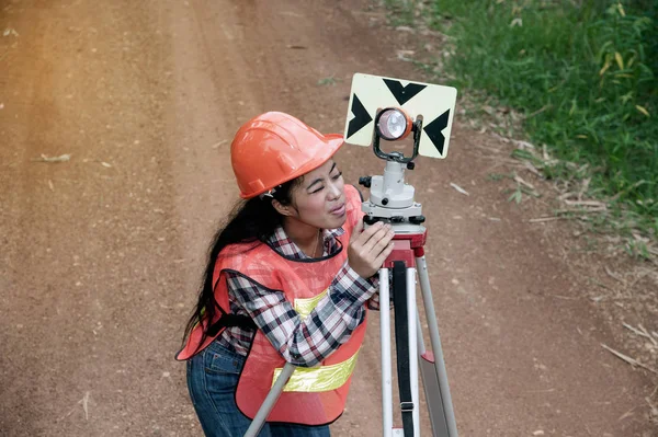 Vrouwelijke Surveyor of ingenieur maken stellen maatregel door prism reflector op straat in een veld. — Stockfoto