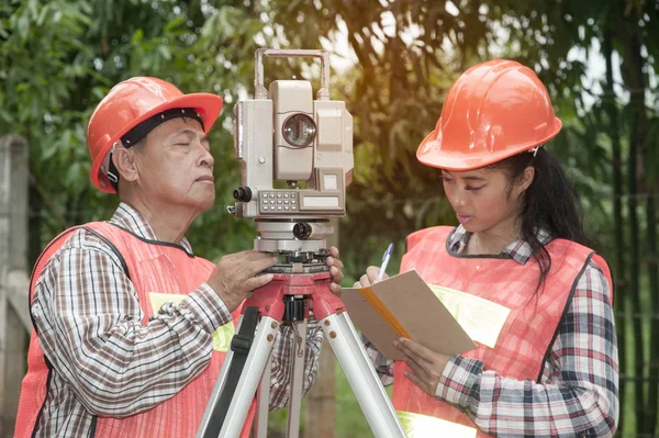 Földmérő, vagy mérnök, így intézkedés teodolit partner az utcán egy mezőben. — Stock Fotó
