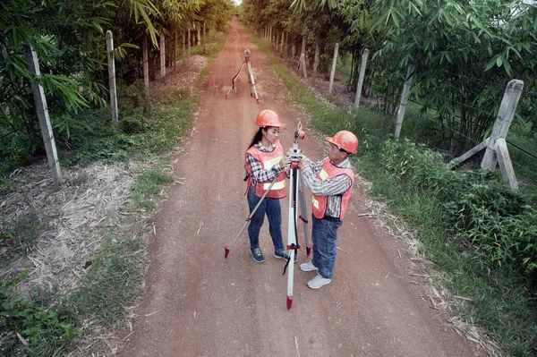 Agrimensor o Ingeniero haciendo medida por Theodolite con socio en la calle en un campo . —  Fotos de Stock