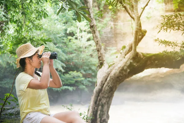 Ganska asiatiska kvinna som tittar med kikare framsidan av vattenfall. — Stockfoto