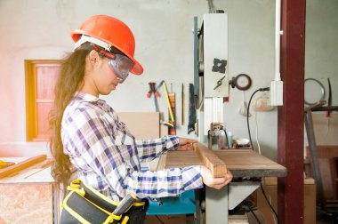 Asyalı güzel kadın marangoz ahşap için elektrikli zımpara kullanarak.