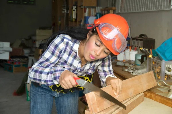 Pretty young Asian  woman using a hand saw to cut some wood.