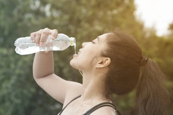 Sporty Asian woman drinking water outdoor after exercise.