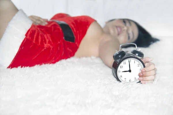 Imagen retrato de una hermosa mujer asiática en Santa Claus roja posando tumbada con reloj en la cama en una habitación . —  Fotos de Stock