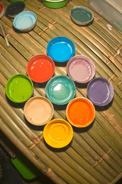 Multicolored plastic cups with paints on bamboo table background — Stock Photo, Image