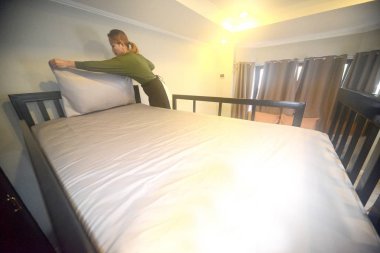 Genç Asya kadın Hostel hizmetçi yatak levha üzerinde beyaz yastık kurma.