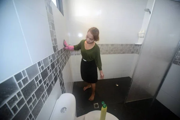 Asiatisk kvinna piga eller hushållerska rengöring på toalett väggen i toaletten. — Stockfoto