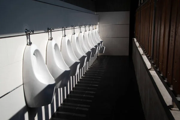 Konst ljus och skugga av mäns toalett med vitt porslin urinaler i linje. Moderna rena offentliga toaletter med kakel. — Stockfoto