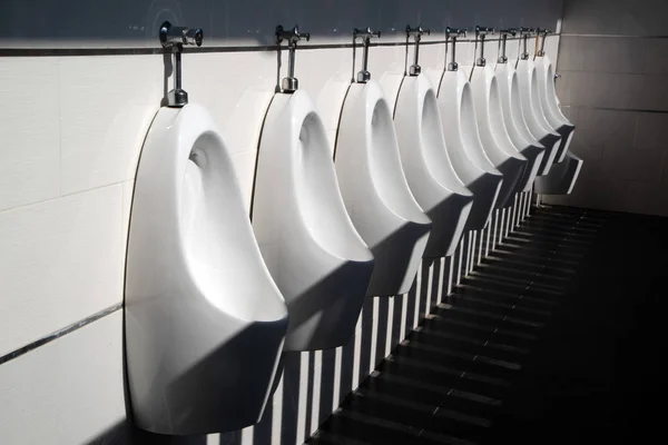 Arte luz e sombra da casa de banho dos homens com mictórios de porcelana branca na linha. Banheiros públicos limpos modernos com azulejos . — Fotografia de Stock