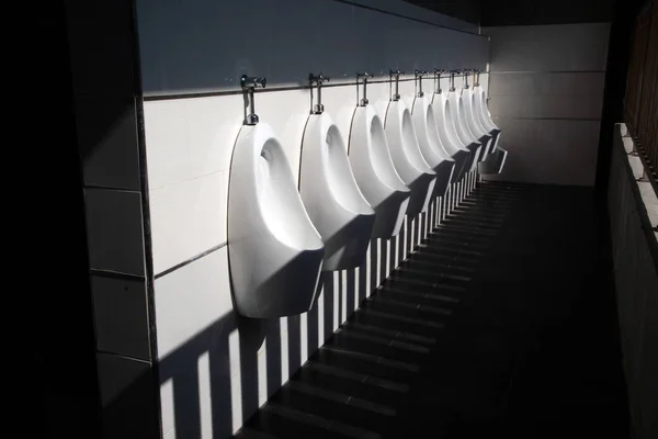 Art light and shadow of men's restroom with white porcelain urinals in line. Modern clean public toilets with tiles. — Stock Photo, Image