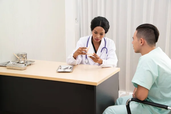 African female dentist holding plastic jaw with orthodontic tools And explained to the male patients. — Stock Photo, Image