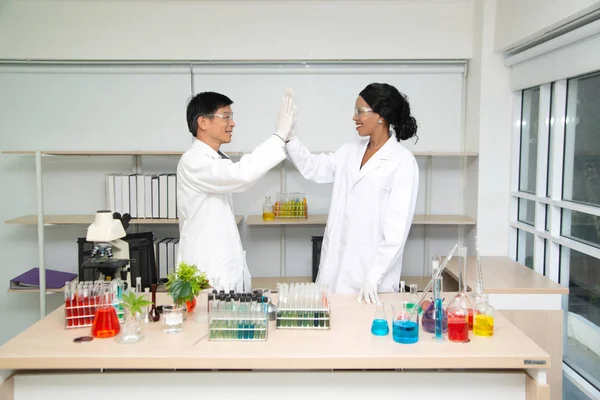 Professionella unga kemister i vita rockar som skakar hand i vetenskapliga laboratorium. — Stockfoto
