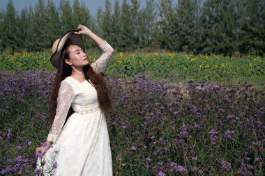 Asyalı güzel bir kadın Verbina Bonariensis çiçek bahçesinde duruyor ve farklı jestlerle eğleniyor.. 