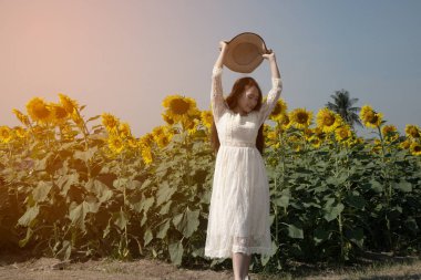 Güzel bir Asyalı kadın imajı, çeşitli jestler ve ayçiçeği tarlasına şapkasını fırlatan eğlenceli ve mutludur.. 