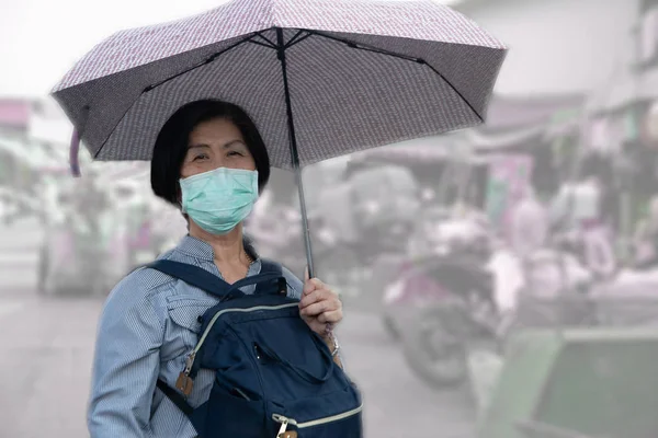 Oudere vrouwen in Azië dragen een Corona Virus en minuut stof pm 2.5 beschermmasker Wandelen en houden paraplu 's rond de markt. — Stockfoto