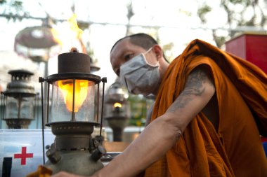 NAKORN PATHOM, THAILAND - 22 Şubat 2020: Kimliği belirsiz Budist keşiş Tayland 'ın Nakorn Pathom Eyaleti' ndeki Don Wai yüzer marketinde 2020 Kasırga Lambası 'nda gösterilecek olan eski kasırga lambasını tamir ediyor..