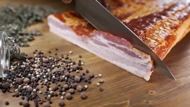 Chef cuts pieces of smoked bacon by sharp knife on the wooden board — Stock Video