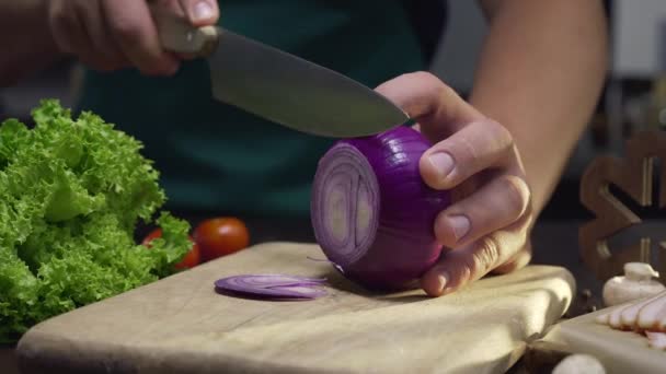 Chef coupe l'oignon rouge par le couteau tranchant sur la planche de bois — Video