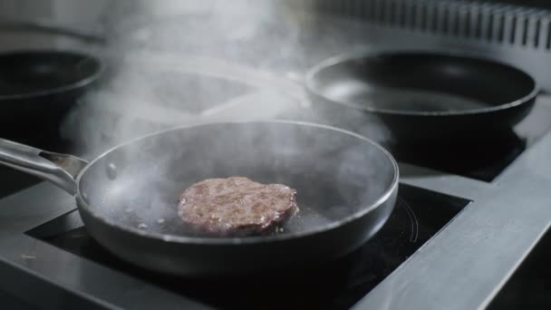 Шеф-повар кладет котлету из сырой говядины на горячую сковороду на кухне ресторана — стоковое видео