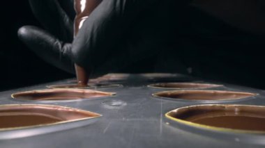 Çikolata kalıplarını pralin için sıvı çikolatayla doldurur.