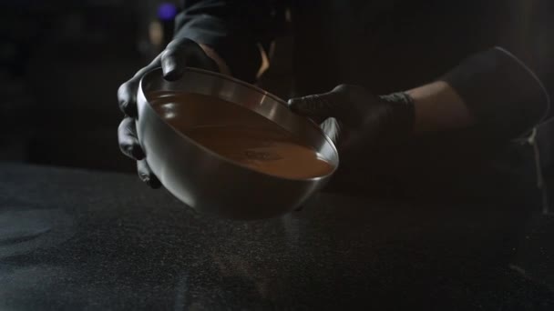 Chocolatier pours melted chocolate from the bowl to the cold table — Stock Video