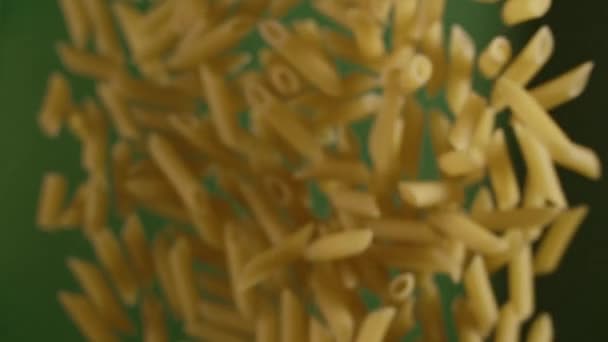 Caída de penne pasta dorada en cámara lenta sobre el fondo verde — Vídeos de Stock