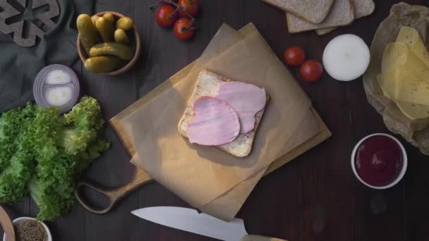Płaskie ułożenie kanapki z szynką w plasterkach i warzywami na drewnianej desce — Wideo stockowe