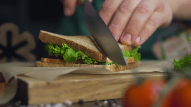 Hombre cortes club sándwich en un medio por cuchillo afilado en una tabla de madera — Vídeos de Stock