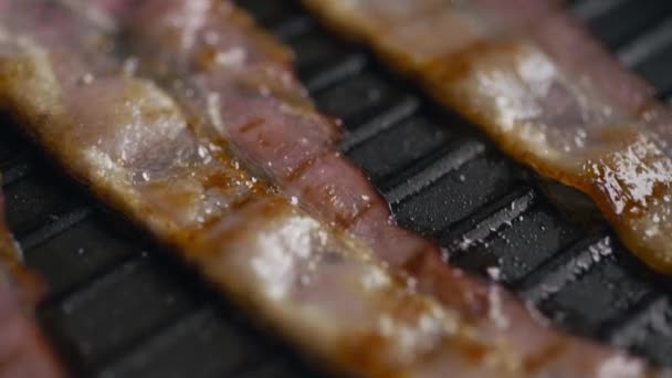 Кусочки бекона поджариваются на горячей сковороде — стоковое видео