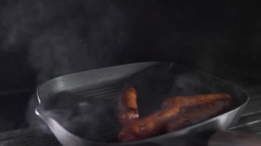 Sosisler ızgara tavasında dumanla kızarıyor.